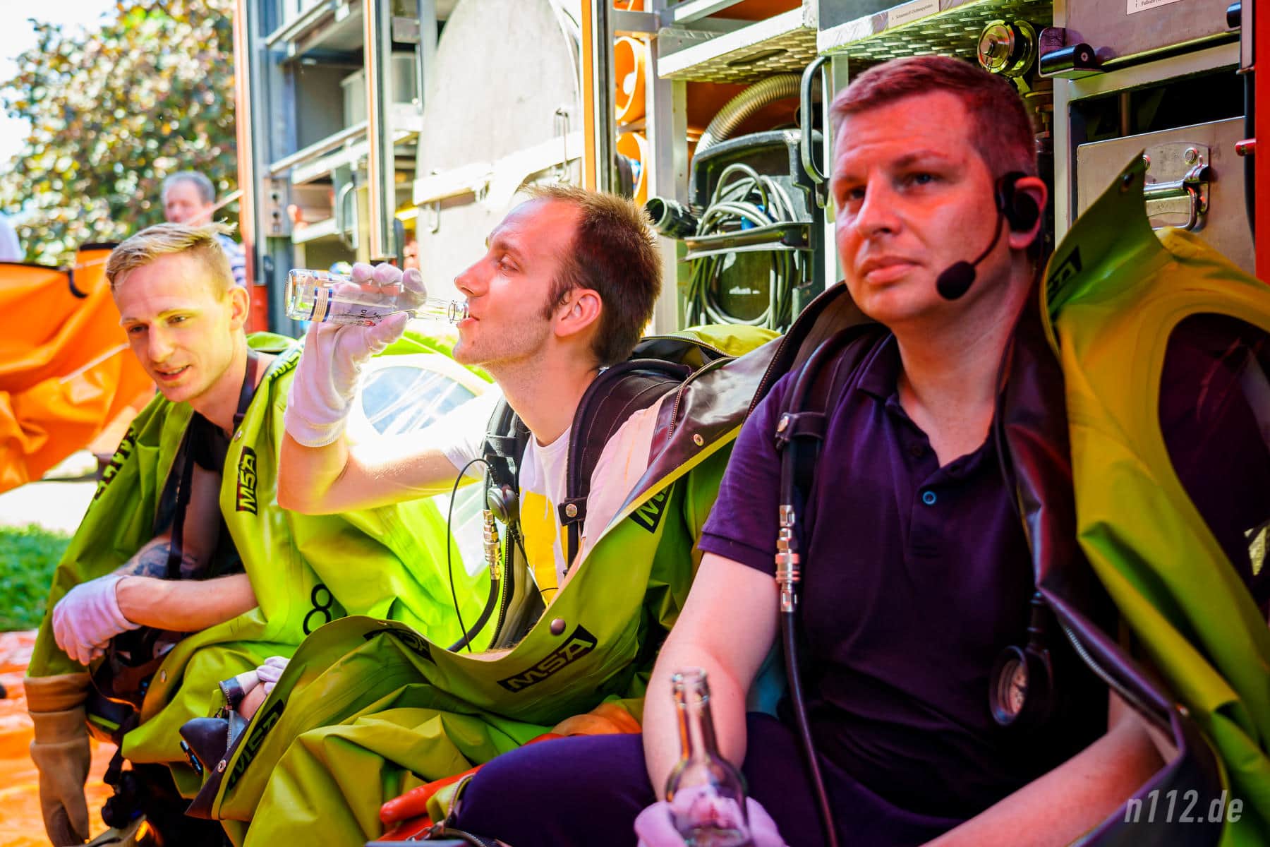 Schon beim Warten schweißgebadet: Ausgerüstet mit Vollschutzanzügen sitzen die Freiwilligen bei 33 Grad im Schatten unter einer Plane (Foto: n112.de/Stefan Hillen)