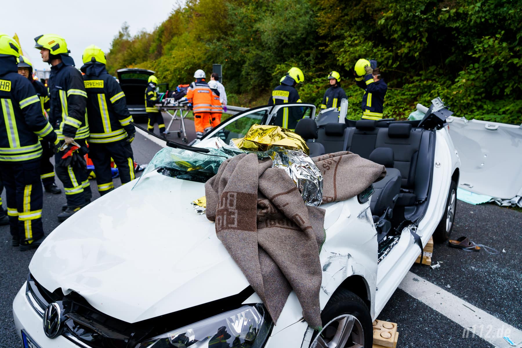 Das Autowrack nach der Rettung. Im Hintergrund wird der Fahrer zum Rettungswagen gebracht (Foto: n112.de/Stefan Hillen)