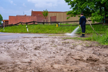 Feuerwehrleute reinigen nach einem heftigen Regenguss die Fahrbahn in Groß Holtensen von Schlamm (Foto: n112.de/Stefan Hillen)