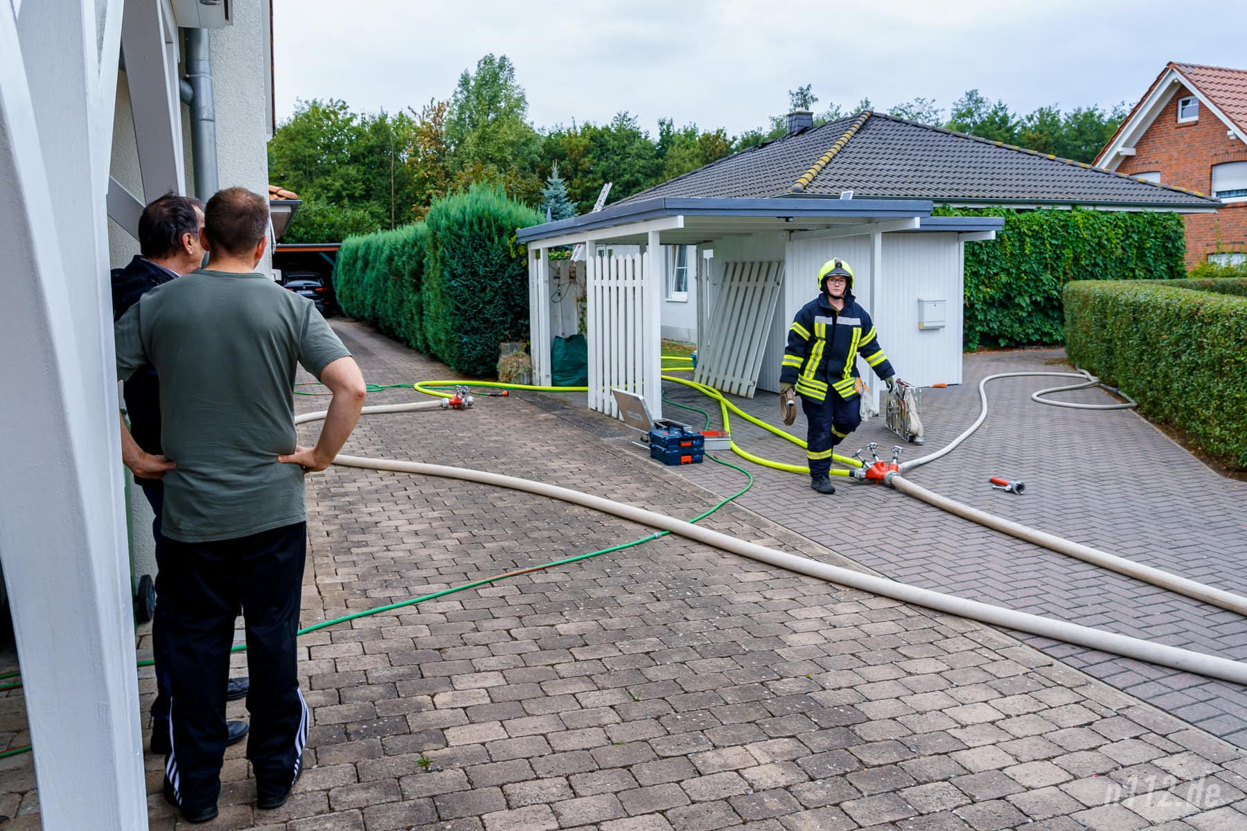 Nachbarn beobachten die Löscharbeiten. Sie hatten die verletzte Frau aus dem Rauch geführt und erste Löschversuche unternommen (Foto: n112.de/Stefan Hillen)